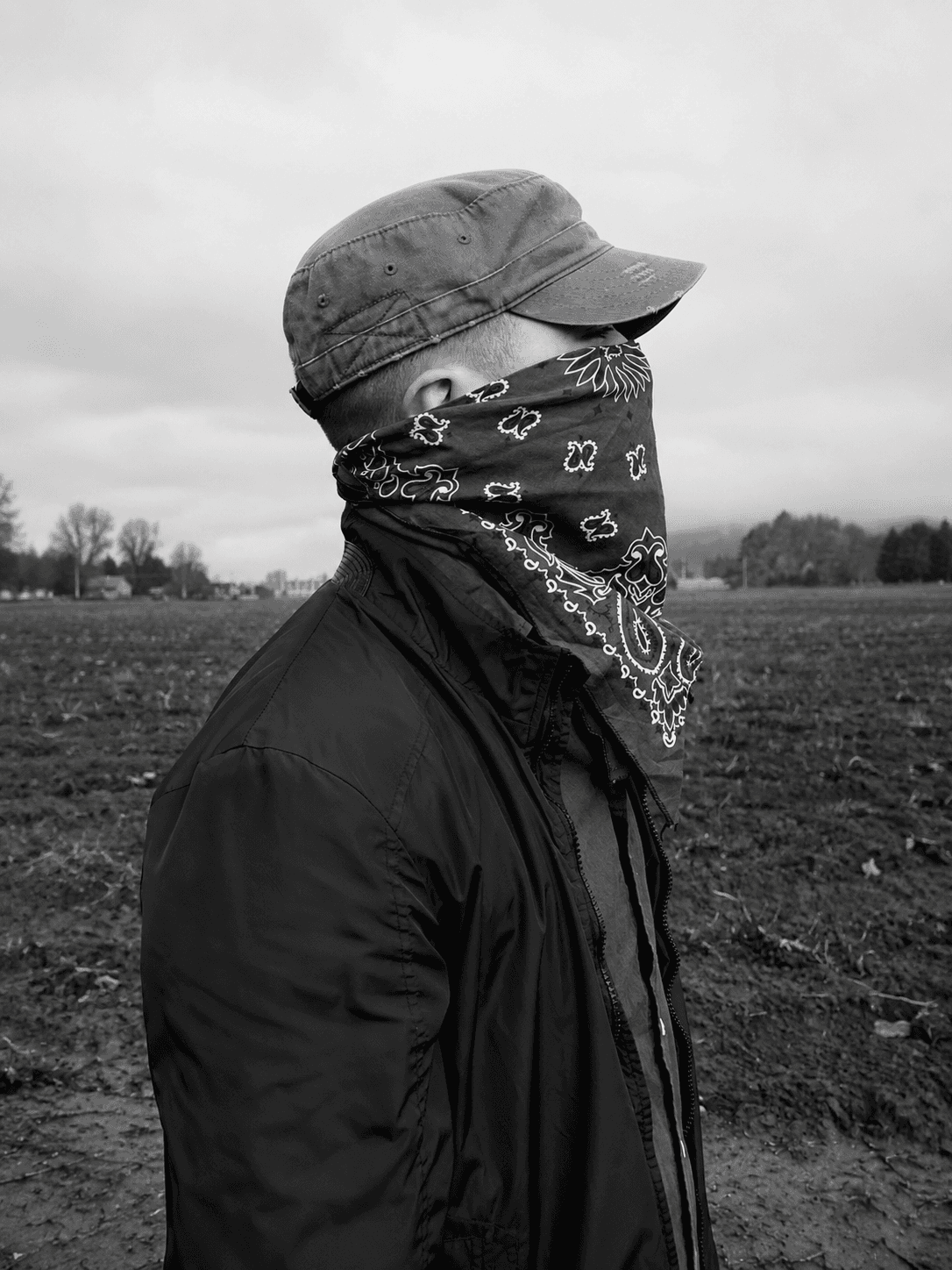 Black-and-white profile portrait in a farm field, representing the founder's roots.